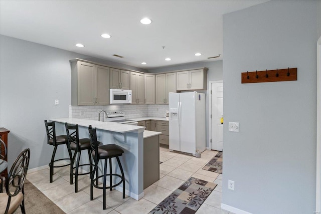 kitchen featuring white appliances, gray cabinets, a peninsula, a kitchen breakfast bar, and decorative backsplash