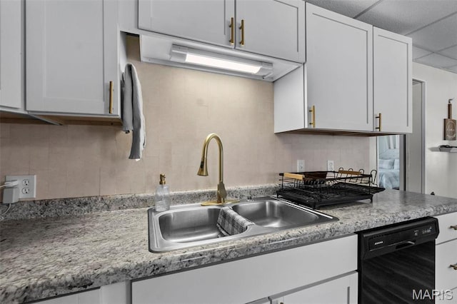 kitchen featuring black dishwasher, a sink, backsplash, and white cabinetry