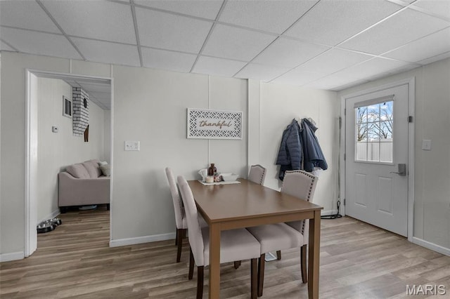 dining space featuring a drop ceiling, light wood-type flooring, and baseboards