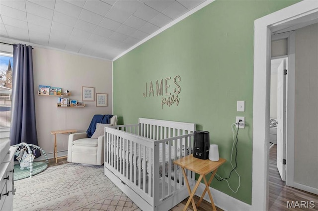 bedroom with wood finished floors, ornamental molding, baseboards, and a nursery area