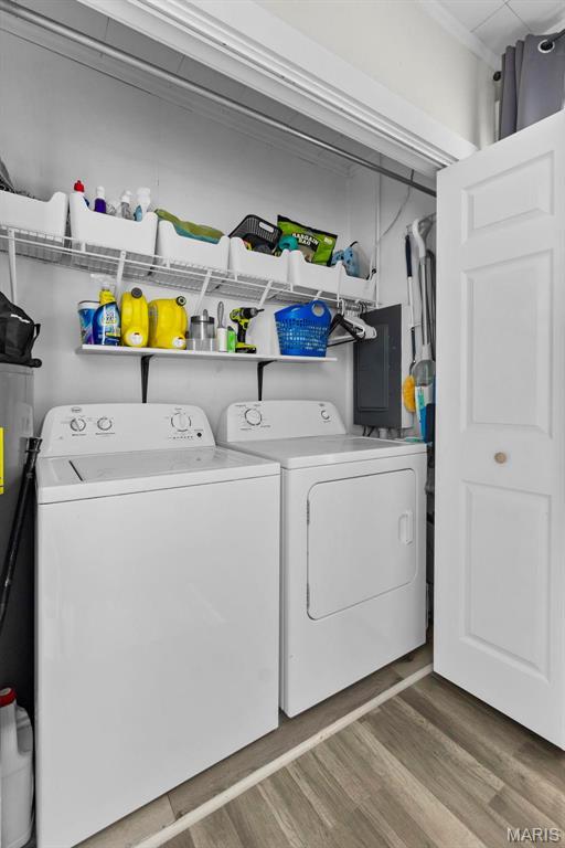washroom with washing machine and clothes dryer, electric panel, and wood finished floors