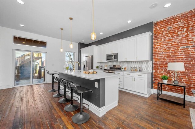 3330 Iowa Ave, Saint Louis, MO 63118 - kitchen with stainless steel appliances, dark wood-style flooring, light countertops, a breakfast bar area, and an island with sink