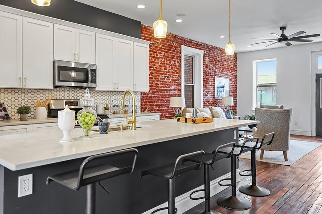 3330 Iowa Ave, Saint Louis, MO 63118 - kitchen with appliances with stainless steel finishes, white cabinets, dark wood finished floors, a breakfast bar area, and recessed lighting