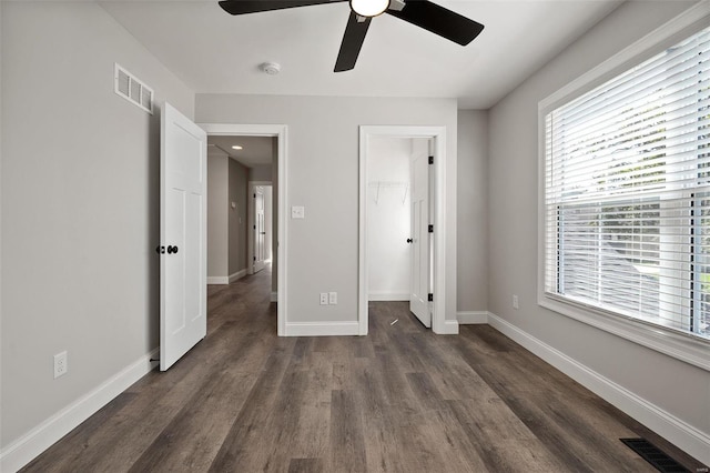 unfurnished bedroom with dark wood-style flooring, a spacious closet, baseboards, and a ceiling fan