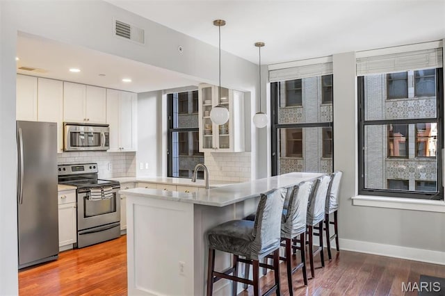 314 N Broadway Unit 903, Saint Louis, MO 63102 - kitchen with appliances with stainless steel finishes, a kitchen breakfast bar, white cabinetry, wood finished floors, and backsplash