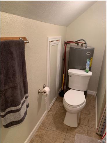 902 S Sutton Pl, Kennett, MO 63857 - bathroom featuring electric water heater, vaulted ceiling, toilet, tile patterned floors, and a textured ceiling