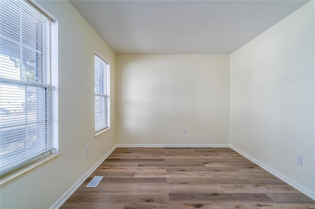 empty room with plenty of natural light, wood finished floors, and baseboards
