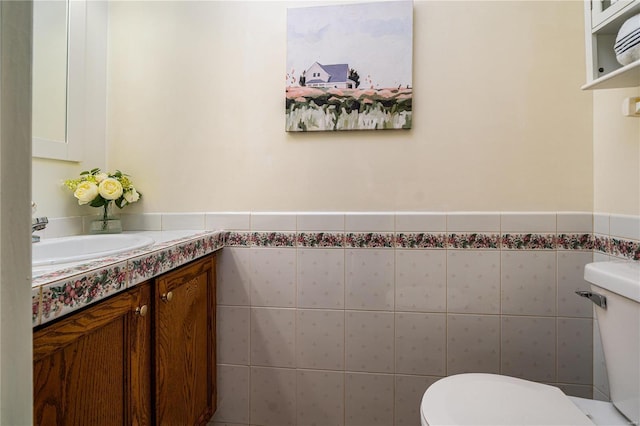 bathroom with toilet, vanity, tile walls, and a wainscoted wall