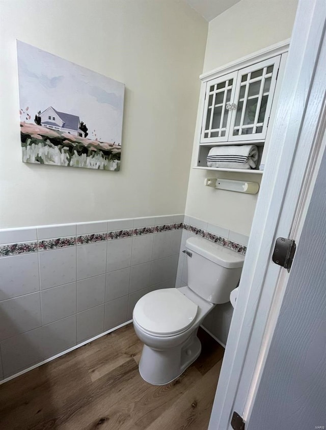 bathroom with wood finished floors, tile walls, toilet, and wainscoting
