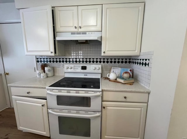 kitchen with double oven range, under cabinet range hood, backsplash, and light countertops