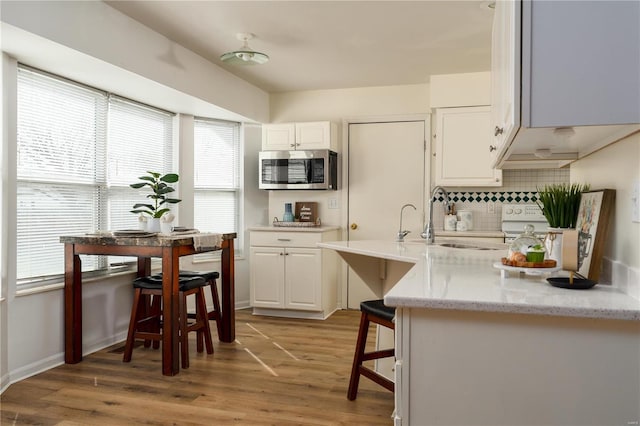 kitchen with stainless steel microwave, white cabinetry, tasteful backsplash, and light wood finished floors