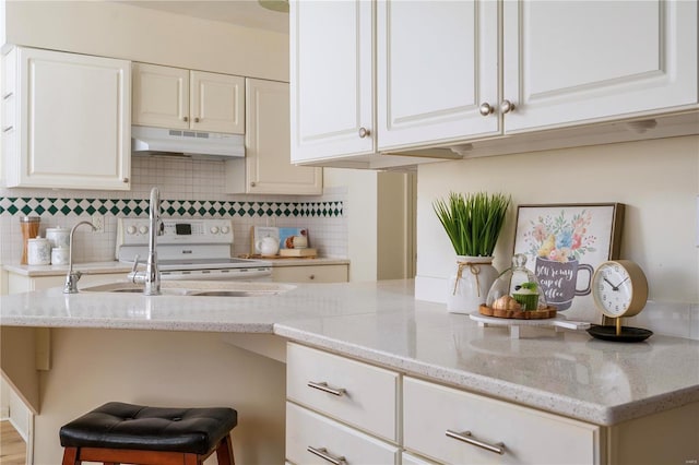kitchen with under cabinet range hood, white electric range, backsplash, light stone counters, and white cabinets