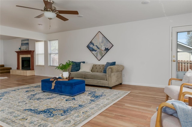 living room with light wood-style flooring, a ceiling fan, baseboards, and a tiled fireplace