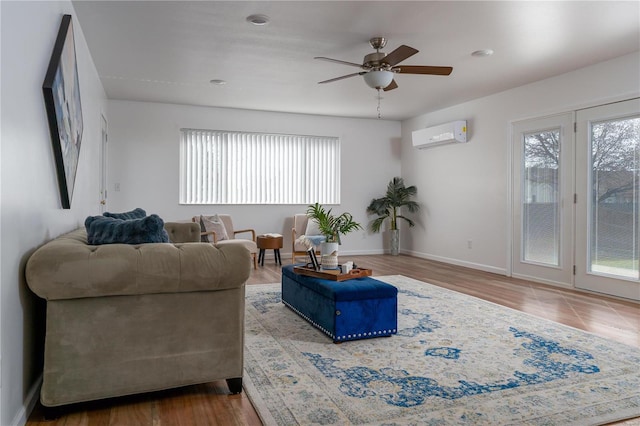living room with ceiling fan, a wall mounted AC, baseboards, and wood finished floors