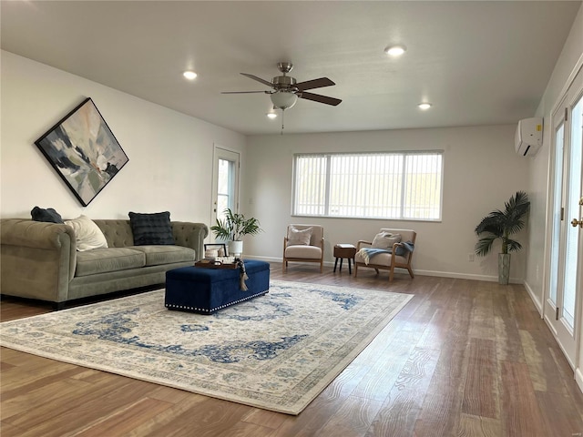 living room with a wall unit AC, baseboards, recessed lighting, ceiling fan, and wood finished floors