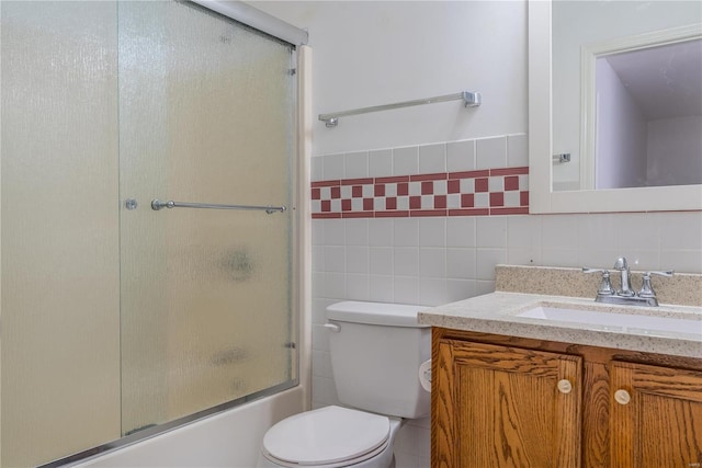 full bathroom with tile walls, vanity, toilet, and bath / shower combo with glass door
