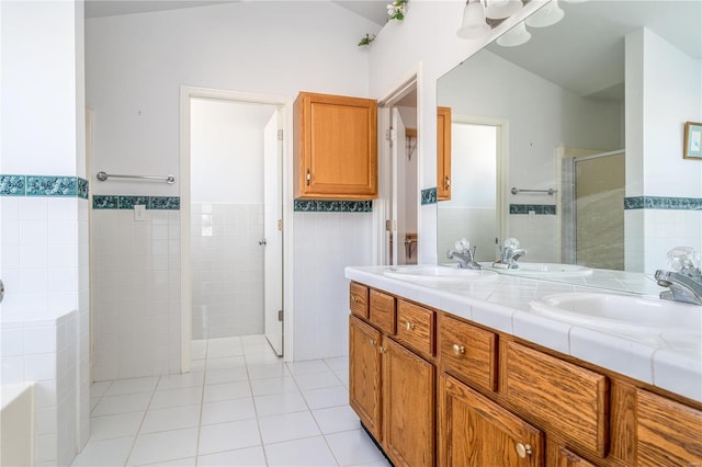 full bath featuring tile walls, a stall shower, tile patterned flooring, double vanity, and a wainscoted wall