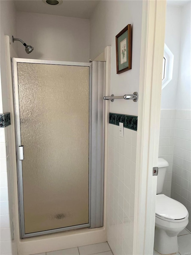 full bath with tile walls, a stall shower, tile patterned flooring, toilet, and a wainscoted wall