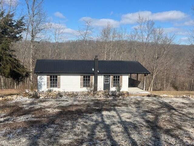 ranch-style home with metal roof, a chimney, an attached carport, and a wooded view