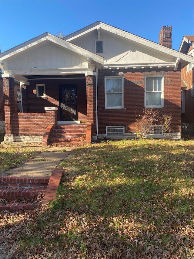 5451 Queens Ave, Saint Louis, MO 63115 - bungalow-style home with brick siding, a chimney, a front lawn, covered porch, and board and batten siding