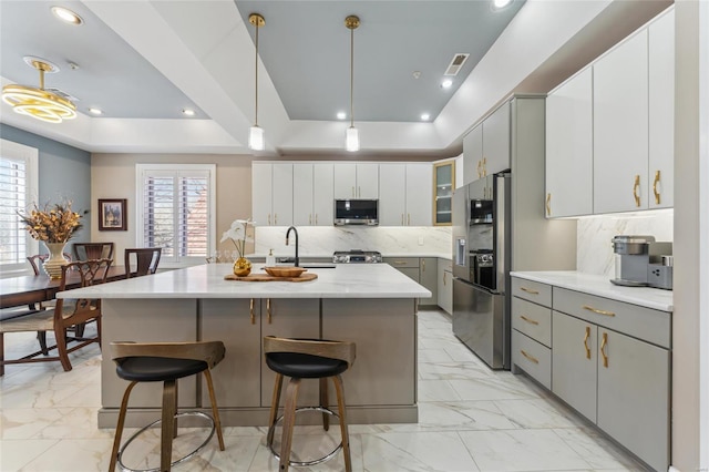 4411 Mcpherson Ave Unit 3, Saint Louis, MO 63108 - kitchen featuring a tray ceiling, gray cabinets, light marble finish floors, stainless steel microwave, and refrigerator with ice dispenser