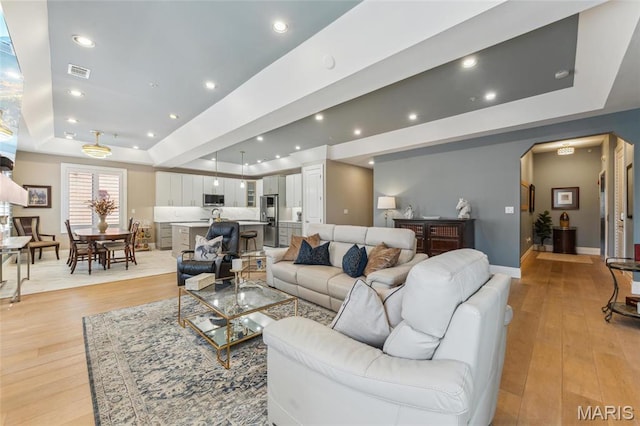 4411 Mcpherson Ave Unit 3, Saint Louis, MO 63108 - living room featuring a tray ceiling, light wood-style flooring, arched walkways, recessed lighting, and baseboards