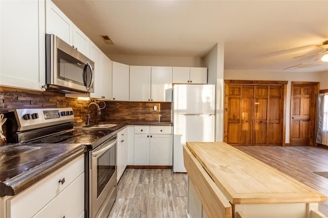 kitchen with appliances with stainless steel finishes, a sink, light wood-type flooring, and tasteful backsplash