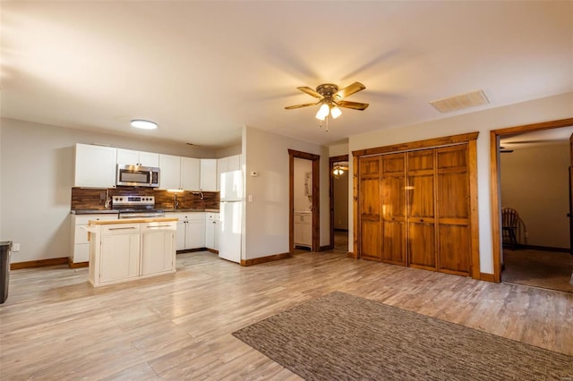 kitchen with appliances with stainless steel finishes, a ceiling fan, baseboards, decorative backsplash, and light wood-style flooring