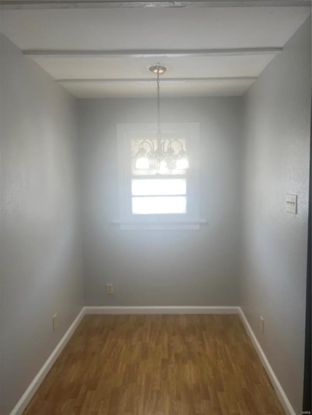 empty room with wood finished floors, baseboards, and a chandelier