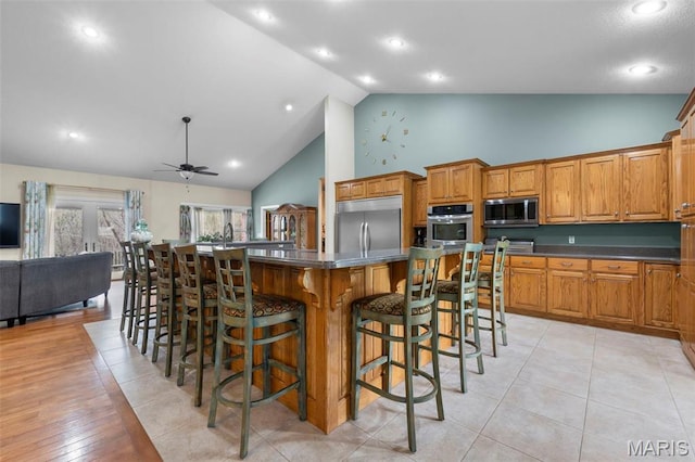 149 Windy Point Ave, Cape Girardeau, MO 63701 - kitchen with appliances with stainless steel finishes, high vaulted ceiling, dark countertops, brown cabinetry, and a breakfast bar