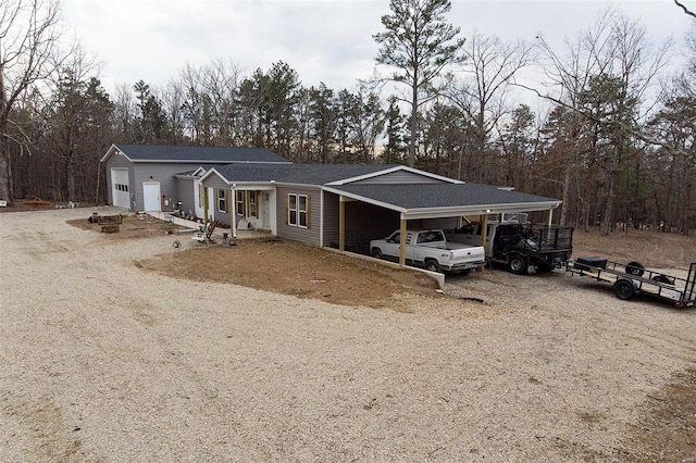 rear view of house with dirt driveway, an attached garage, a shingled roof, and a carport