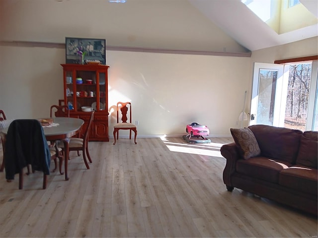 living room with light wood-style flooring, vaulted ceiling, baseboards, and a skylight