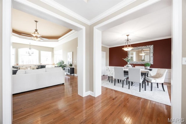 dining space with hardwood / wood-style floors, ornamental molding, a ceiling fan, a raised ceiling, and baseboards