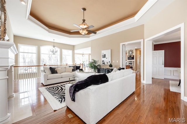 living room with a tray ceiling, a chandelier, a ceiling fan, crown molding, and wood finished floors