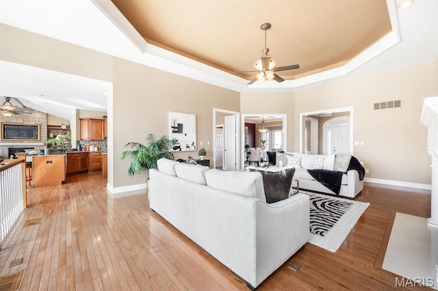 living room featuring a ceiling fan, a tray ceiling, light wood-style flooring, and baseboards