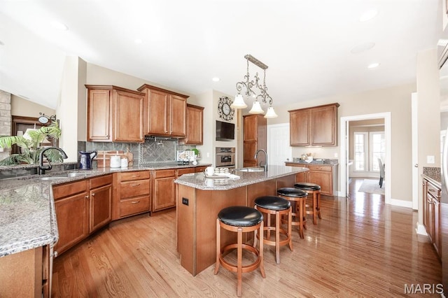 kitchen with a sink, light wood-style floors, brown cabinetry, vaulted ceiling, and recessed lighting