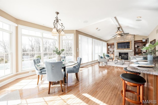dining area featuring a fireplace, light wood-type flooring, a ceiling fan, vaulted ceiling, and healthy amount of natural light
