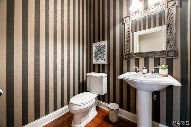 half bathroom featuring wood finished floors, baseboards, and toilet