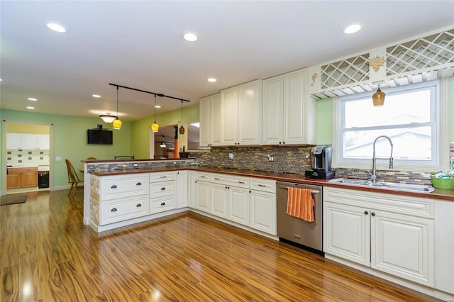kitchen featuring stainless steel dishwasher, a sink, dark countertops, a peninsula, and tasteful backsplash