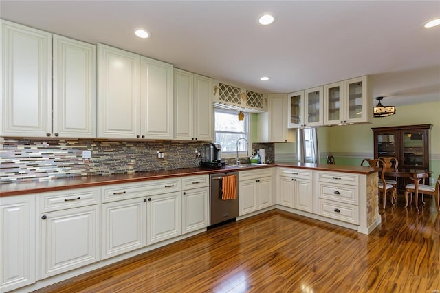 kitchen with dishwasher, a peninsula, a sink, wood finished floors, and backsplash