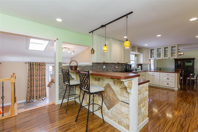 kitchen with a peninsula, dark wood-style floors, glass insert cabinets, dark countertops, and a kitchen breakfast bar