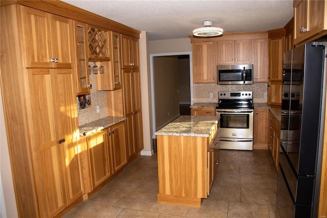 kitchen featuring appliances with stainless steel finishes, a center island, tasteful backsplash, light stone countertops, and a textured ceiling