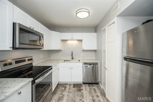 kitchen with appliances with stainless steel finishes, a sink, light wood-style flooring, and white cabinetry