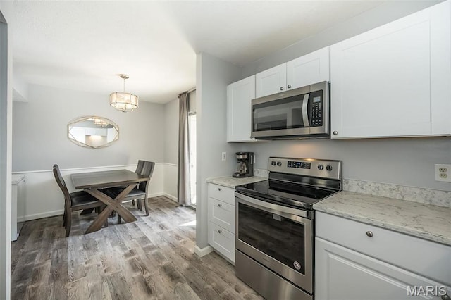 kitchen with stainless steel appliances, wood finished floors, white cabinets, light stone counters, and hanging light fixtures