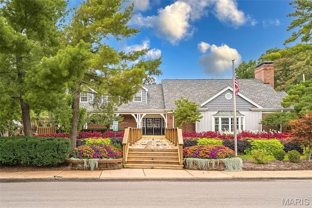 view of front of property with board and batten siding, a chimney, brick siding, and a shingled roof