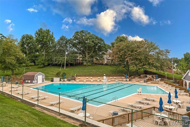 community pool featuring a patio area, a storage shed, and view of wooded area