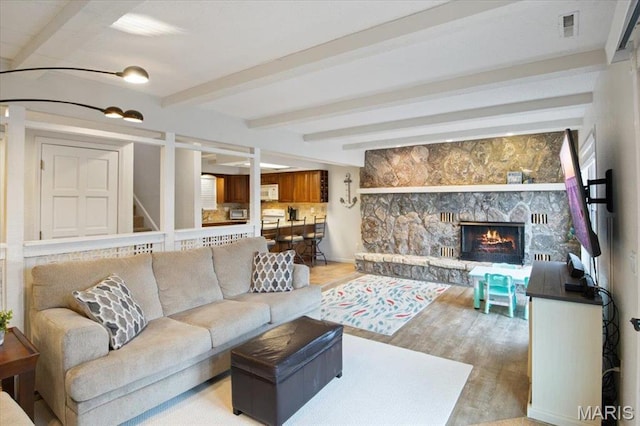 living area with beamed ceiling, light wood-type flooring, and a fireplace