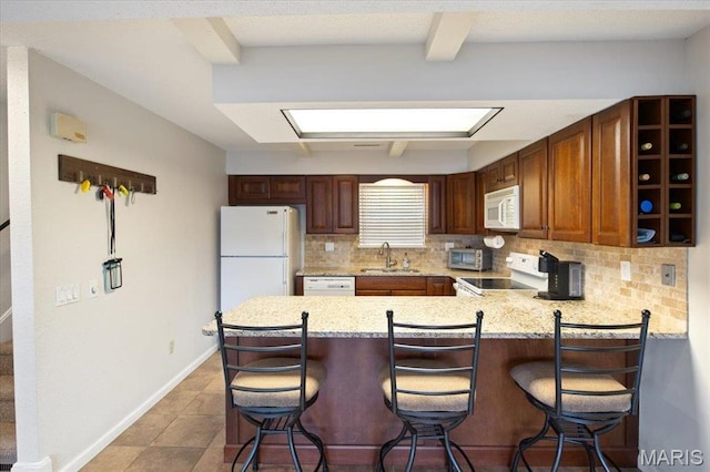 kitchen with white appliances, a sink, decorative backsplash, a peninsula, and a kitchen bar