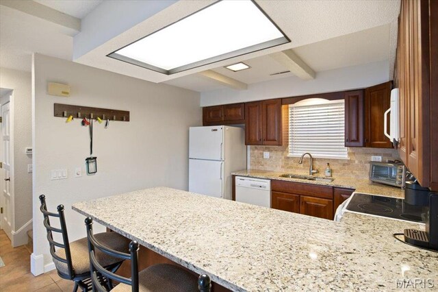 kitchen with a sink, white appliances, a peninsula, backsplash, and light stone counters