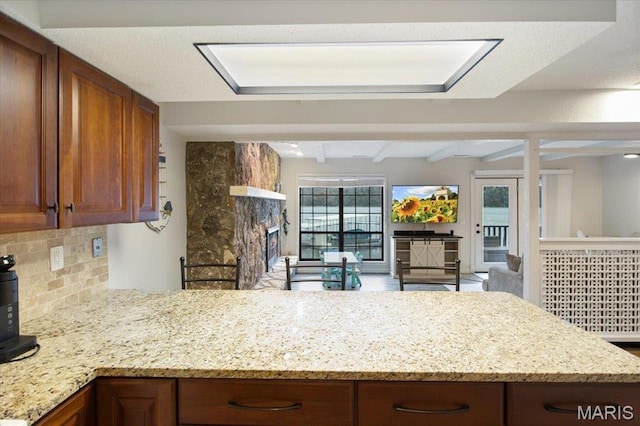 kitchen with backsplash, light stone counters, a peninsula, beamed ceiling, and a fireplace